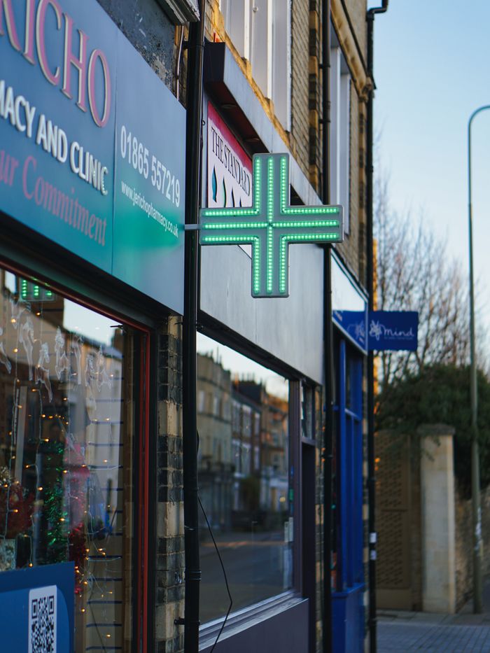 A pharmacy storefront with neon sign in Oxford, England's urban street view.